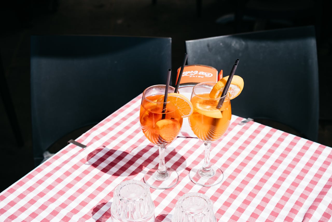 Two Aperol Spritz cocktails on a checkered tablecloth outdoors in the sun.